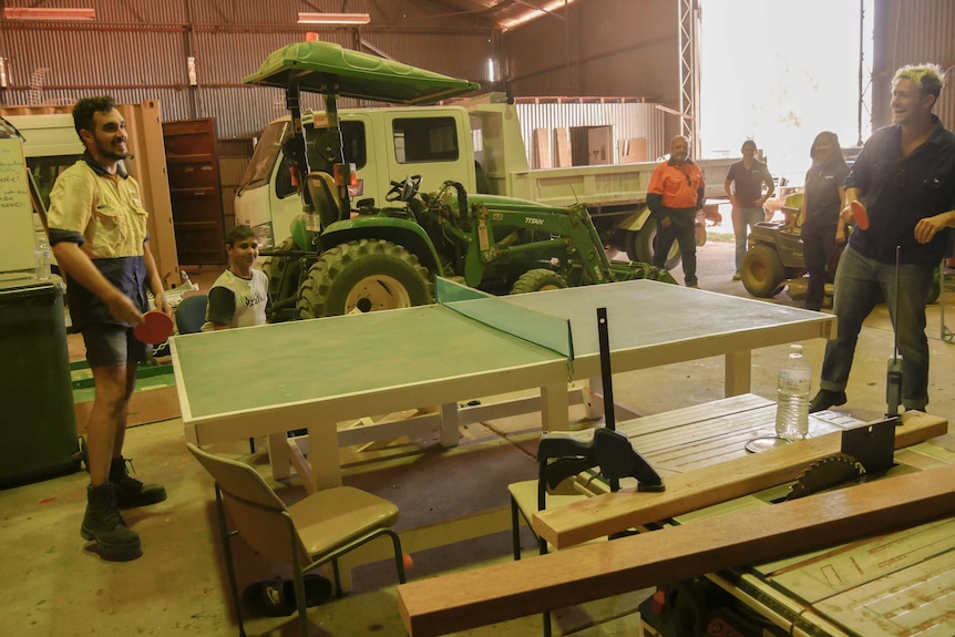 Two young men playing table tennis inside a large shed