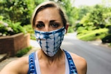 A young woman standing on a leafy street in a blue and white face mask