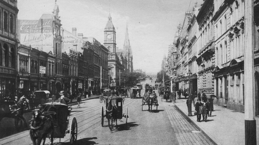 A black and white image of a busy city street in Melbourne, in 1875. The street is full of horse buggies.