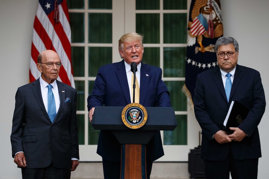 President Donald Trump speaks from behind a podium as Commerce Secretary and Attorney General stand by his sides.