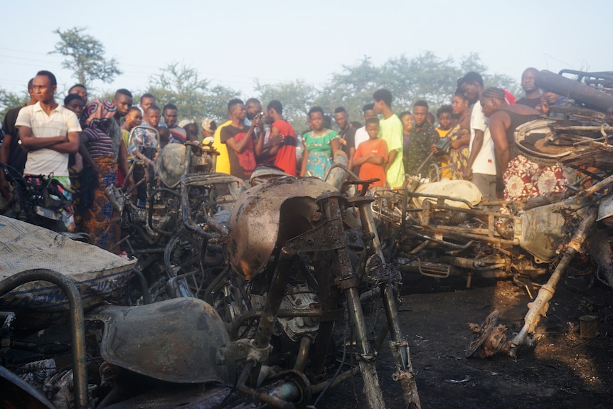 People look on at a pile of burnt motorbikes.