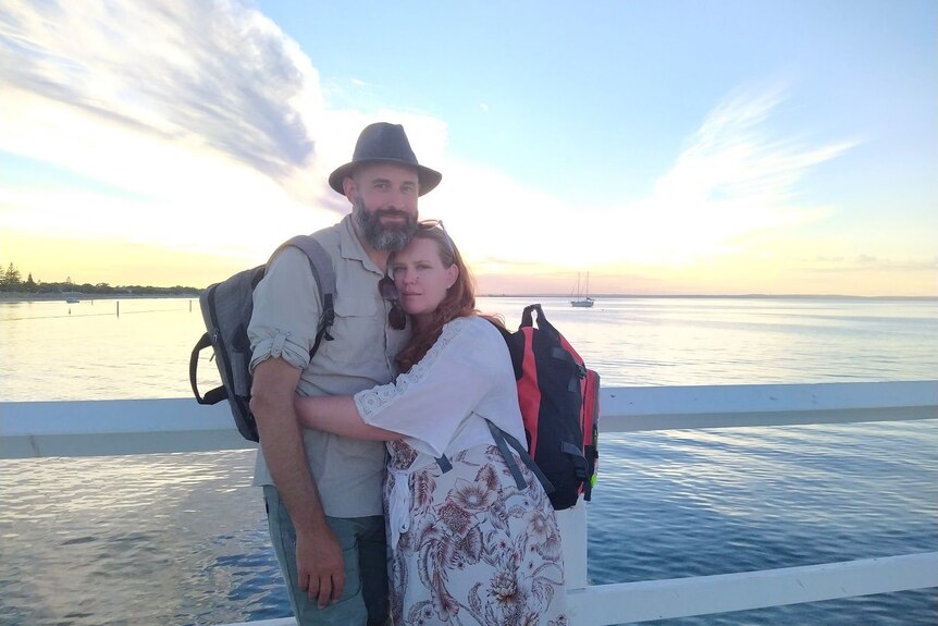 Sheree and Paul Willems stand on a jetty with sunset in background.