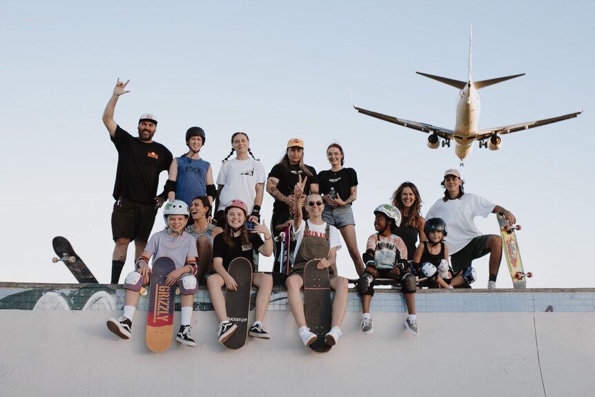 group of people with skateboard waving as plane lands in background