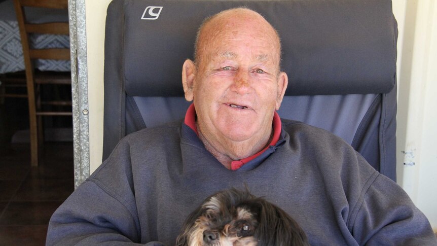 Dick Kingdom, looking relaxed, sitting in a chair with a dog on his lap.