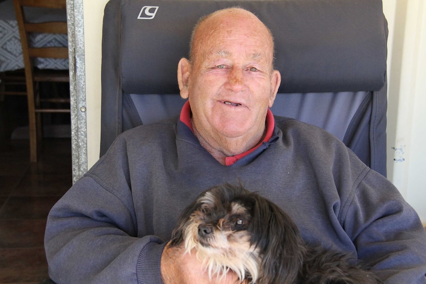 Dick Kingdom, looking relaxed, sitting in a chair with a dog on his lap.