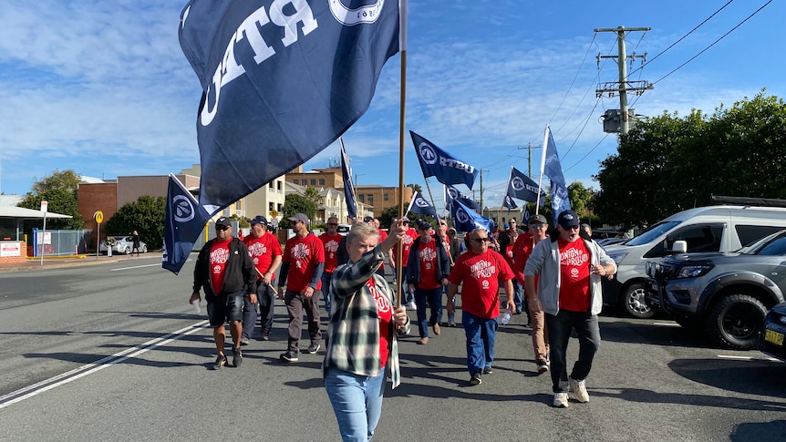 Bus drivers marching, wearing red shirts, waving a flag.