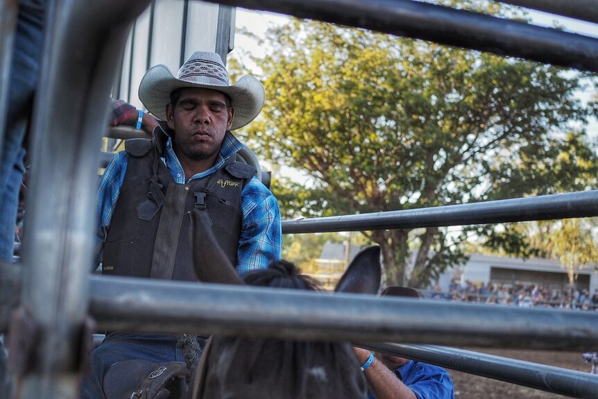 A rider closes his eyes in concentration before he is let loose into the ring at the Fitzroy Crossing Rodeo.