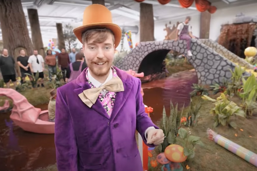 A man in a Willy Wonka costume stands in front of a chocolate river.