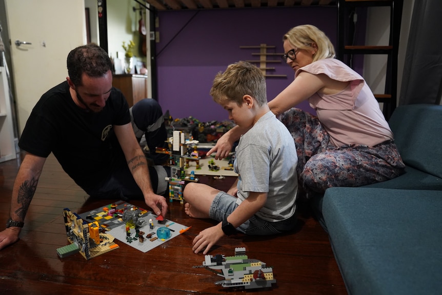 A boy sits with his parents playing Lego.