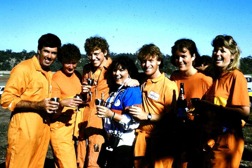 A group of six male and female pilots wearing blue uniforms drink out of chalices with Director Ruth Wilson wearing a blue shirt