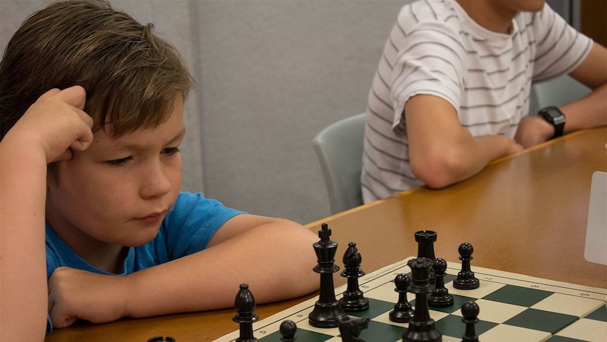 Nine-year-old Brock Anderson stares at a chess board, mid-game.