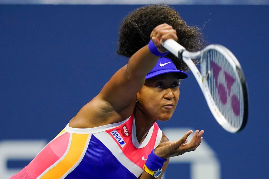 Naomi Osaka looks forward with her racquet above her head as she completes her service action