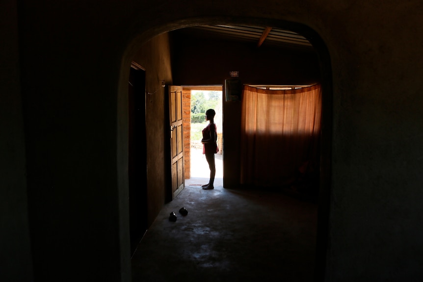 The shadow of a young woman standing side-on in a doorway looking outside.