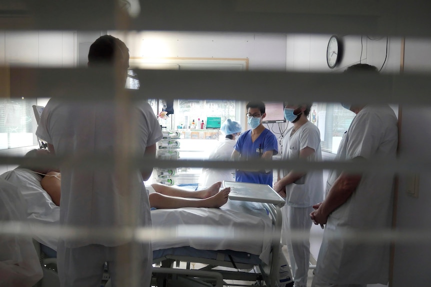 Medical staff stand around the bed of a COVID-19 patient