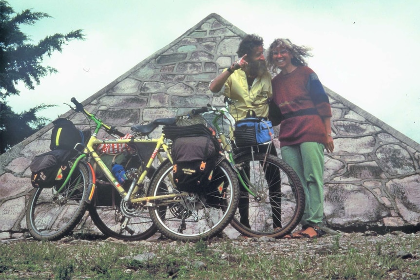 Man and woman with packed bicycles standing in front of a pyramid