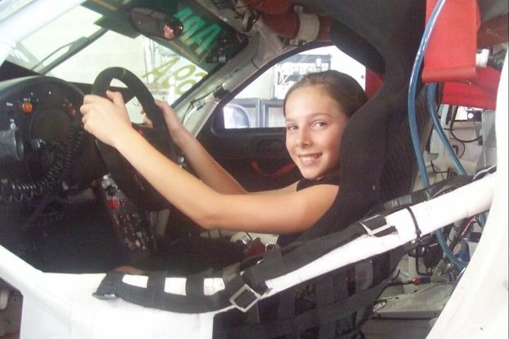 A young girl sitting in the driver's seat of a race car.