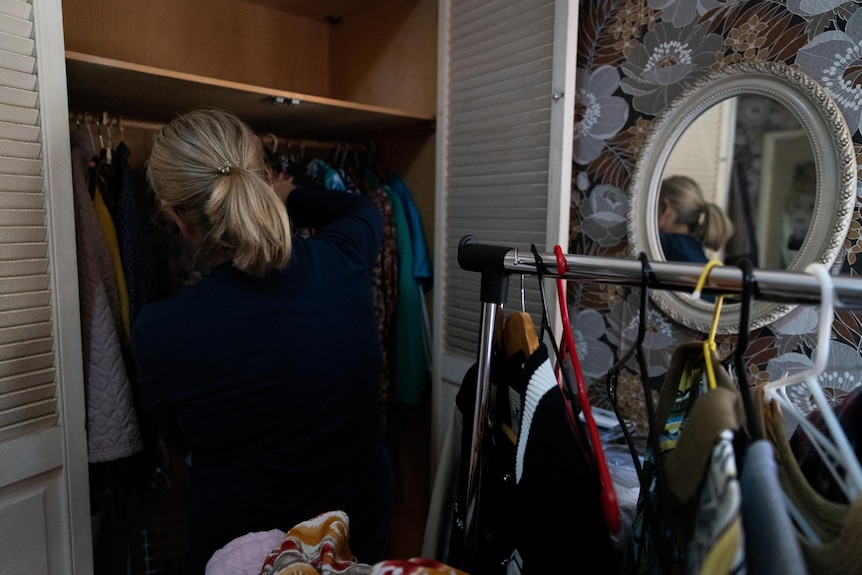 A woman sifts through an old cupboard full of clothes.