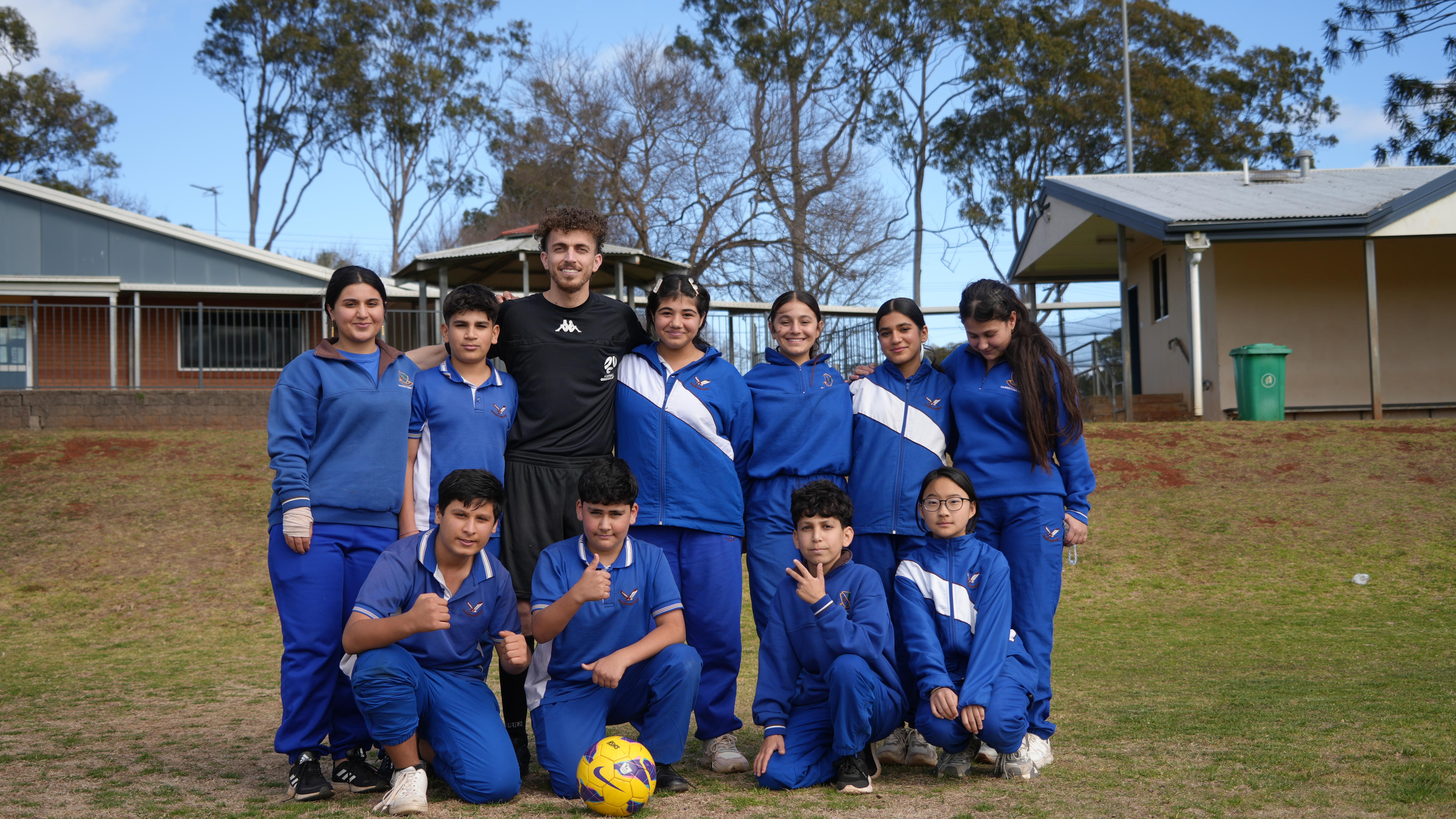 Smiling man with students and soccer ball.