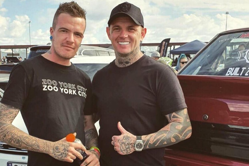 Two men with heavily tattooed arms standing next to one another and smiling