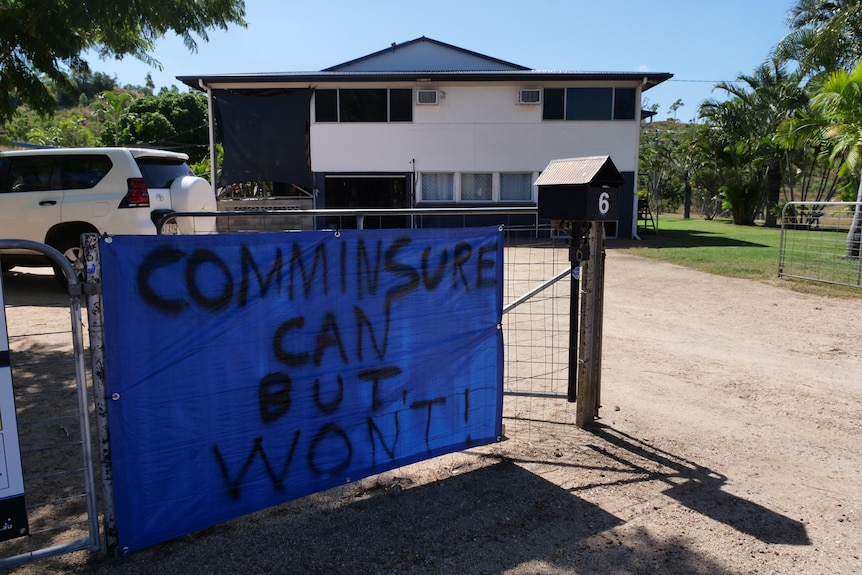 a house behind a fence where a sign saying "CommInsure can but won't" is hung on the fence