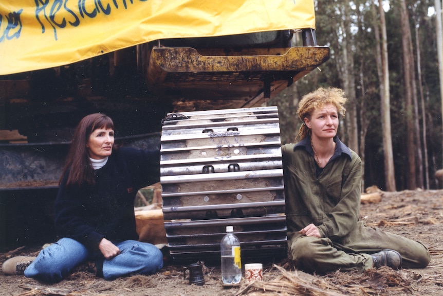 Two women have arms locked onto machinery.