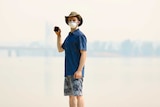 A man stands wearing a mask in thick smoke, holding an air quality monitor.