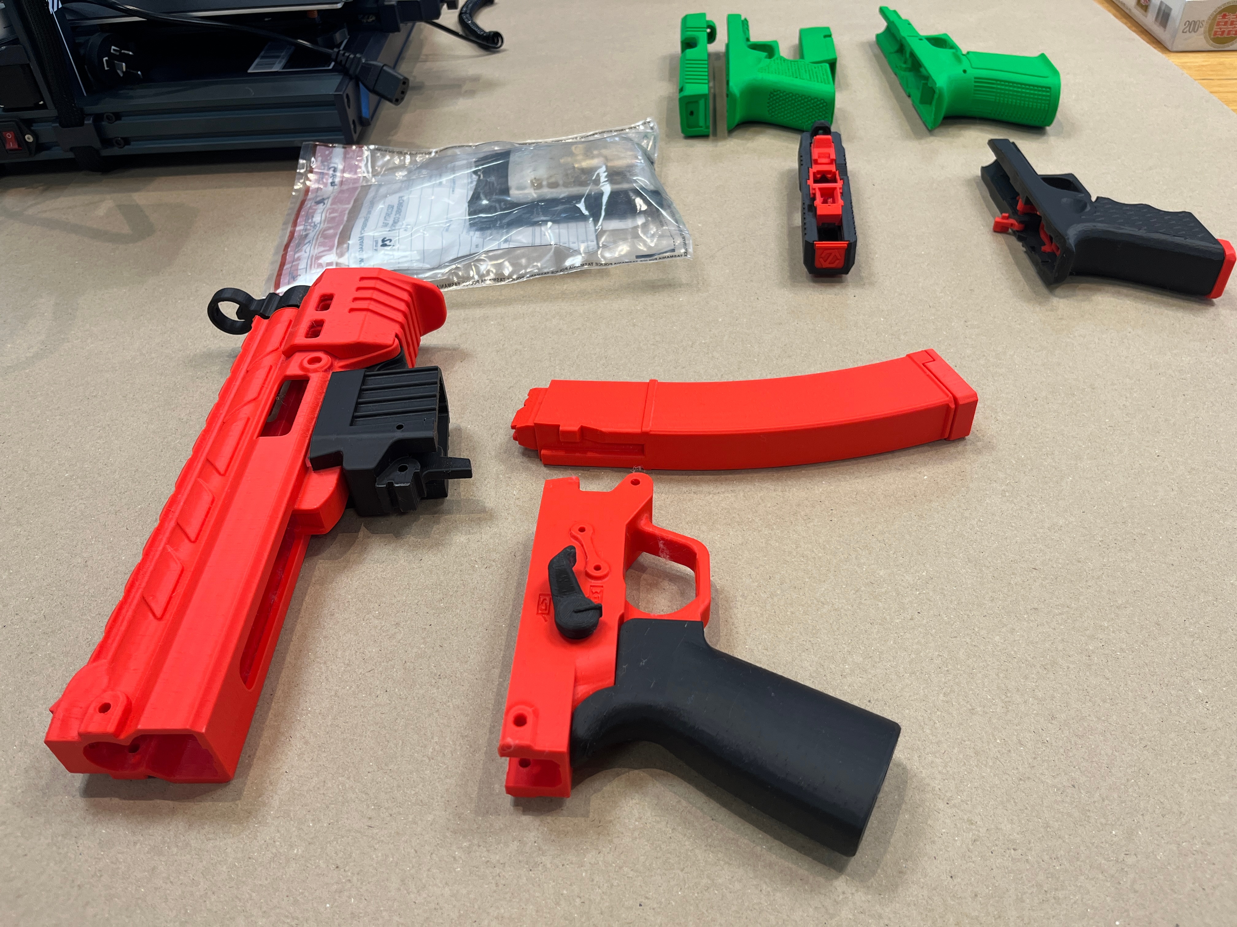 A red 3D printed firearm on a wooden table.