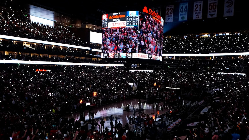 An NBA arena lies in near-darkness, as fans use lights from their mobile phones to see during a playoff game.