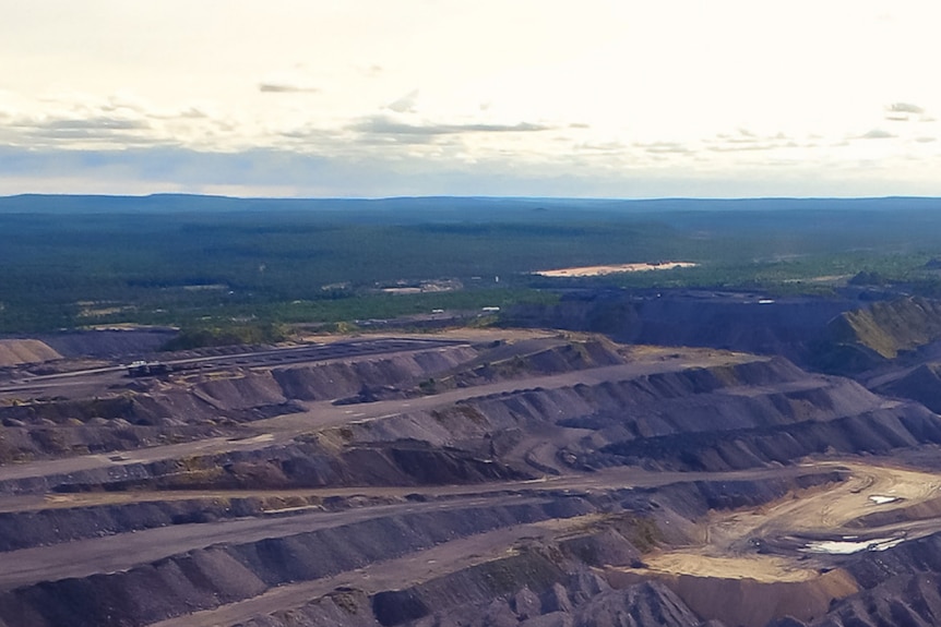 An aerial view of an open cut mine with ridges of dark earth on display with a sparse green horizon in the background