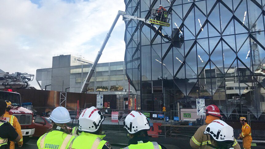 Emergency services on the ground look up at men stuck in a cherry picker