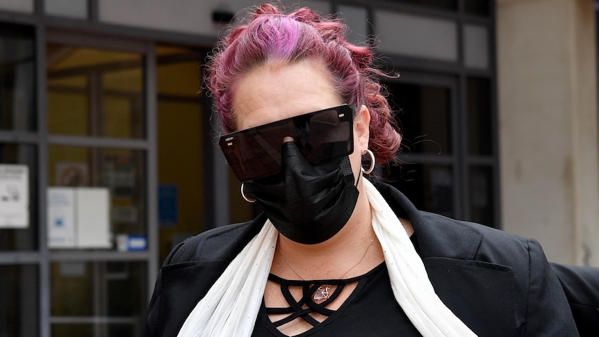 A woman with purple hair wearing sunglasses and a face mask