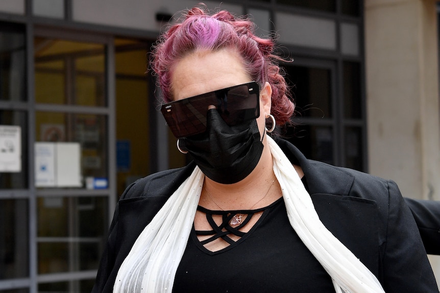 A woman with purple hair wearing sunglasses and a face mask