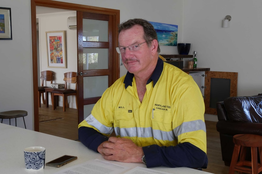 He wears a high-vis shirt and sits in his living room at a table