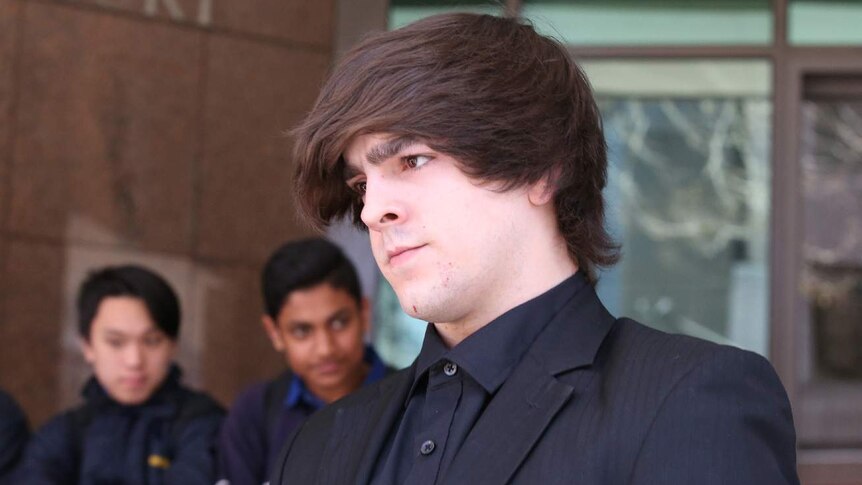 Zachery Larkins wears a black suit and black shirt outside the court doors.