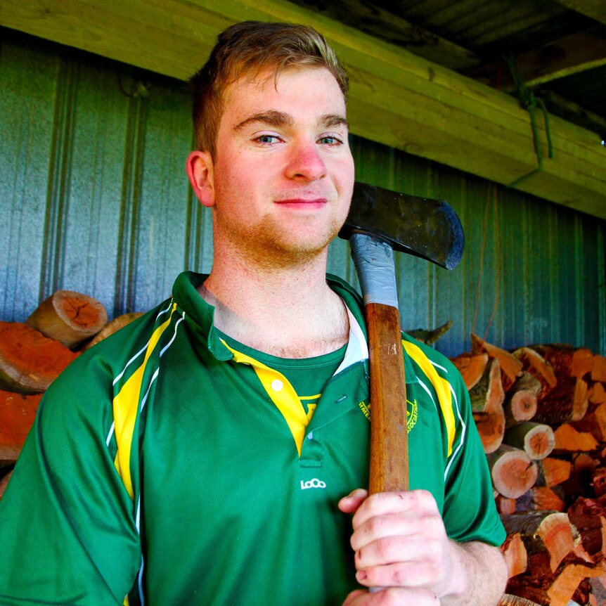 young man standing in front of pile of wood with axe