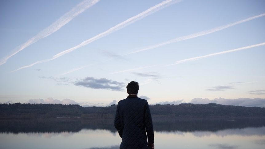 A man with a camera standing in front of a sky full of contrails.