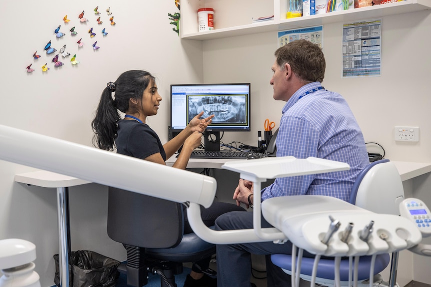 A woman and a man huddle around a computer screen showing an x-ray of teeth.