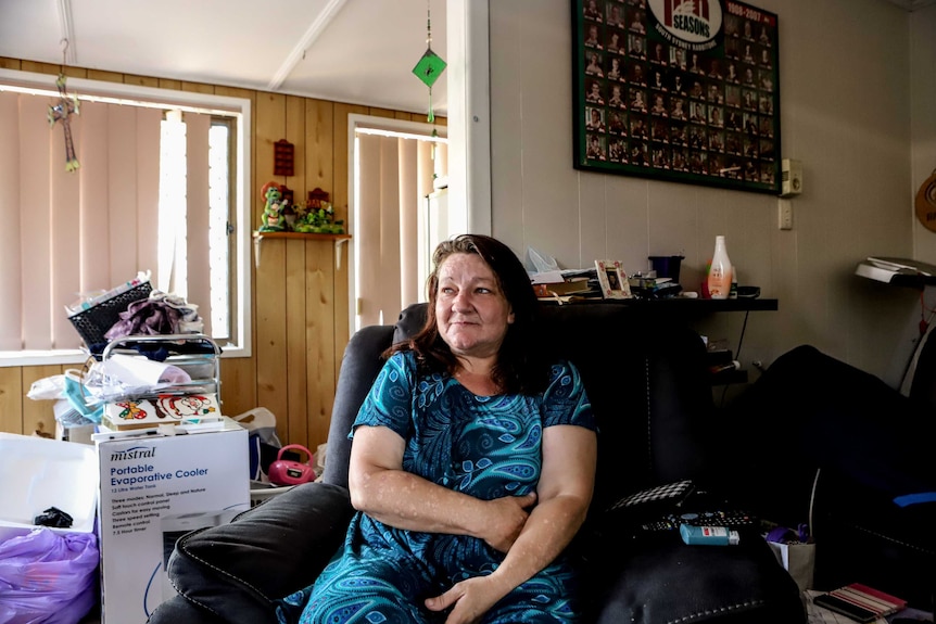 Lisa Baker, sitting on chair inside a loungeroom with shut blinds behind her.