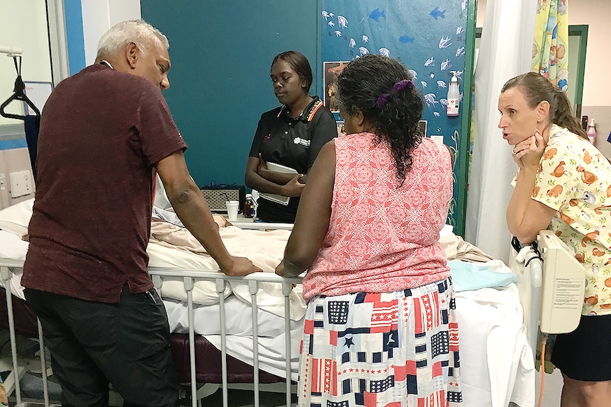 Four people standing around hospital bed.