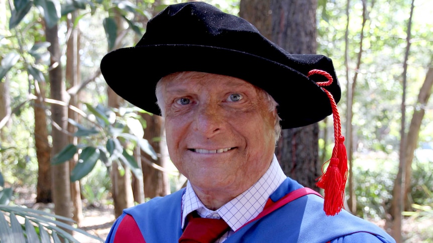 Dr Robert Sawyer stands in academic gown in bushland.