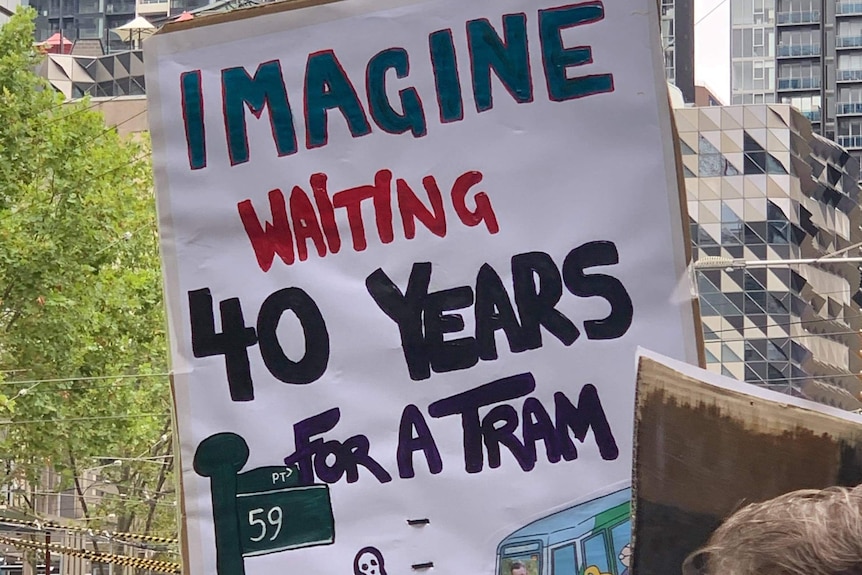 Protesters stand near a tram with a sign that reads 'imagine waiting 40 years for a tram'. 