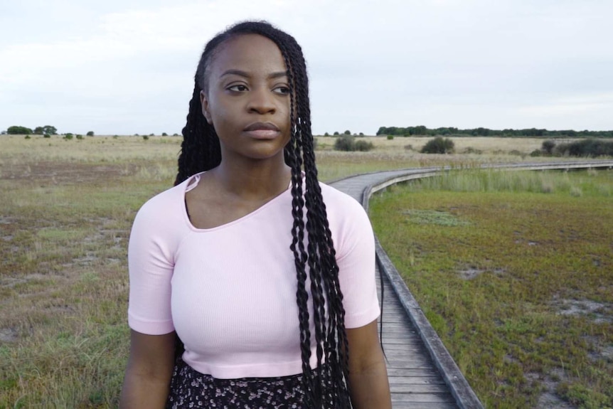 A young woman walking along a raised walkway outside looking into the distance