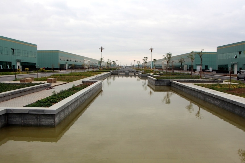 Large green warehouses in two rows separated by a man-made creek