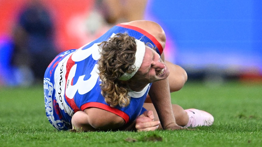 AFL player Aaron Naughton, lying on the ground, clutching his right knee, screaming in pain