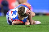 AFL player Aaron Naughton, lying on the ground, clutching his right knee, screaming in pain
