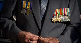 An image of an unidentified war veteran buttoning a jacket, medals on display.