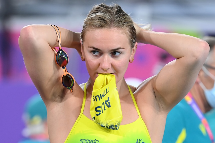 Ariarne Titmus holds her hair and bites a swim cap