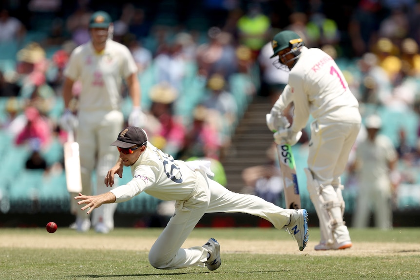 England fielder Joe Root dives for a cricket ball hit by Australia's Usman Khawaja (blurred in the background).