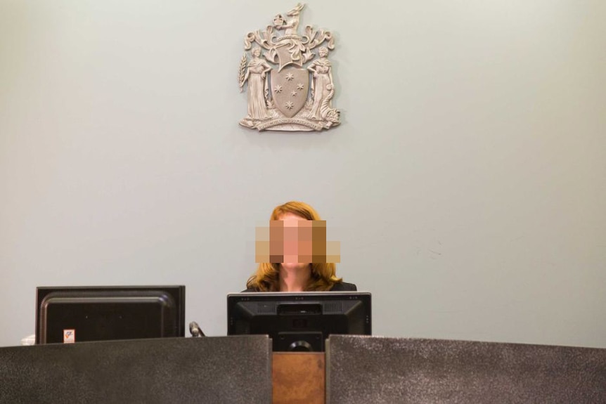 A woman sits under a coat of arms with a blurred face