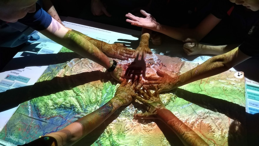 Several hands reach across a hologram of a map